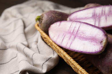 Photo of Purple daikon radishes in wicker basket on wooden table, closeup. Space for text