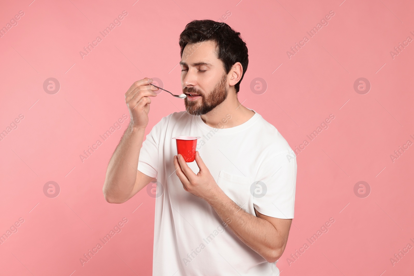 Photo of Handsome man eating delicious yogurt on pink background