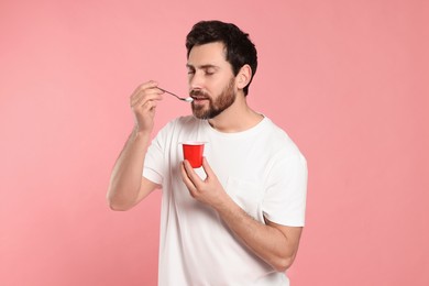 Photo of Handsome man eating delicious yogurt on pink background