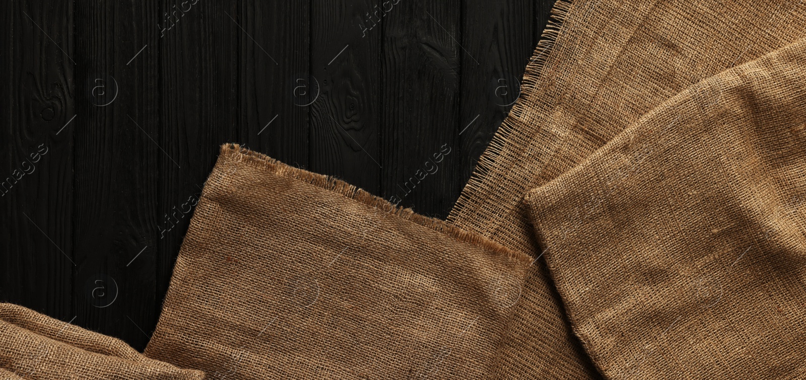 Photo of Burlap fabric on black wooden table, top view. Space for text