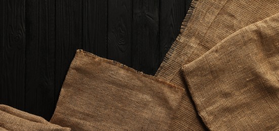 Photo of Burlap fabric on black wooden table, top view. Space for text