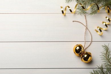 Photo of Golden sleigh bells, serpentine streamers and fir branches on white wooden background, flat lay. Space for text