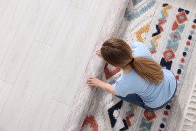 Woman unrolling carpet with beautiful pattern on floor in room, top view. Space for text