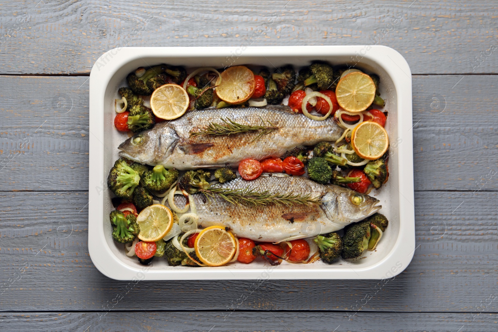 Photo of Delicious fish with vegetables and lemon in baking dish on grey wooden table, top view