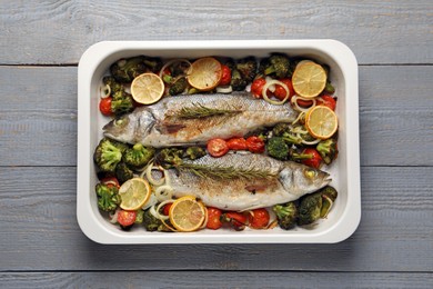 Photo of Delicious fish with vegetables and lemon in baking dish on grey wooden table, top view