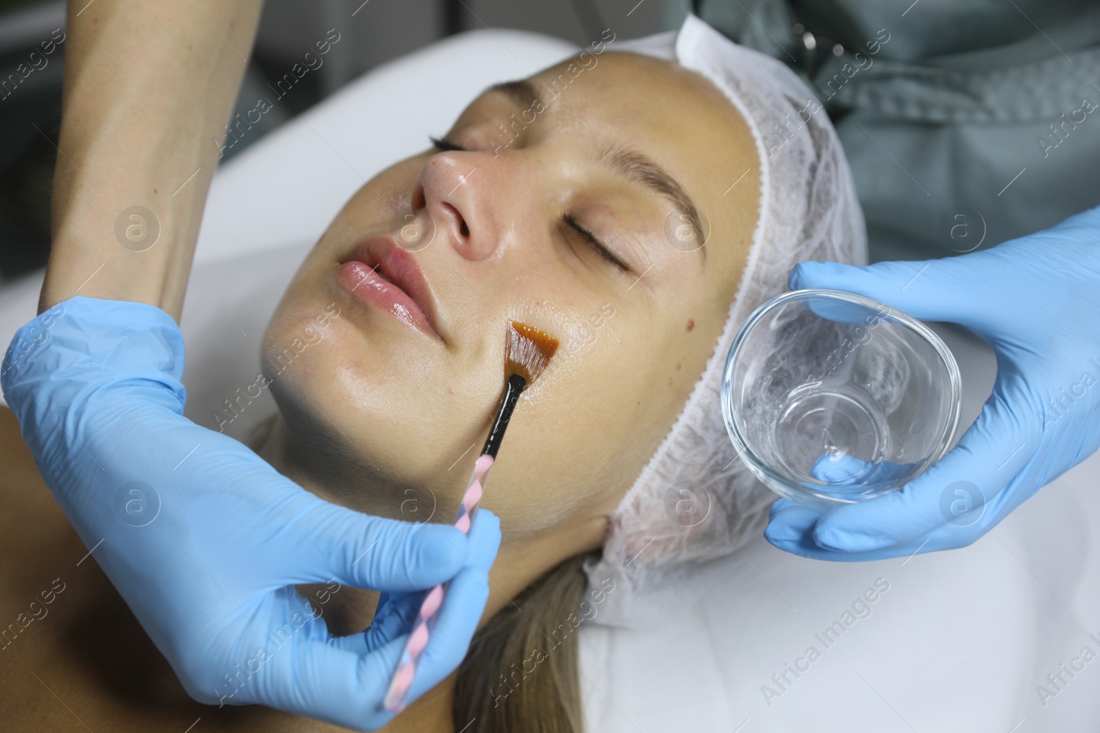 Photo of Cosmetologist applying cosmetic product for chemical peeling on client's face in salon