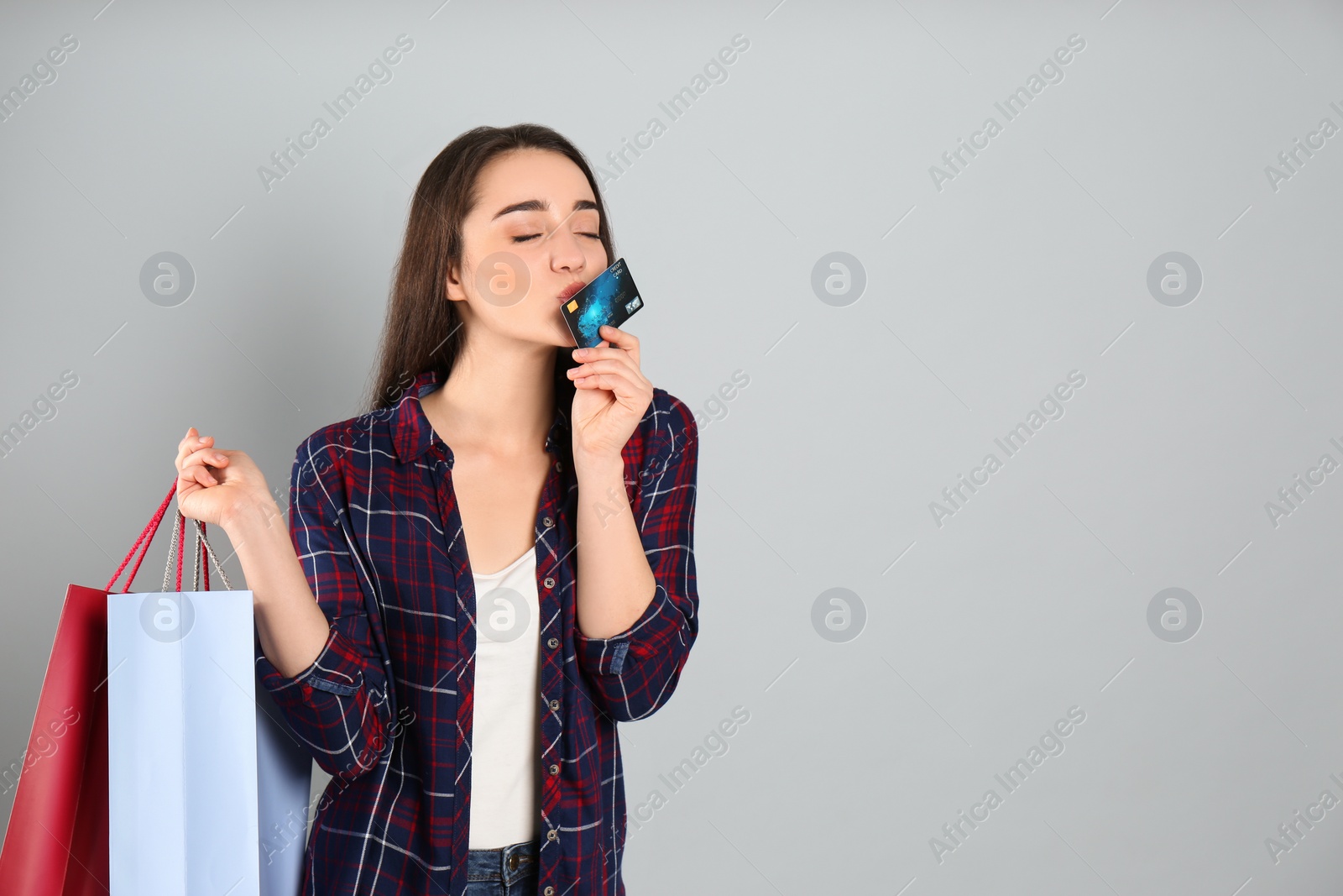 Photo of Young woman with credit card and shopping bags on light grey background, space for text. Spending money