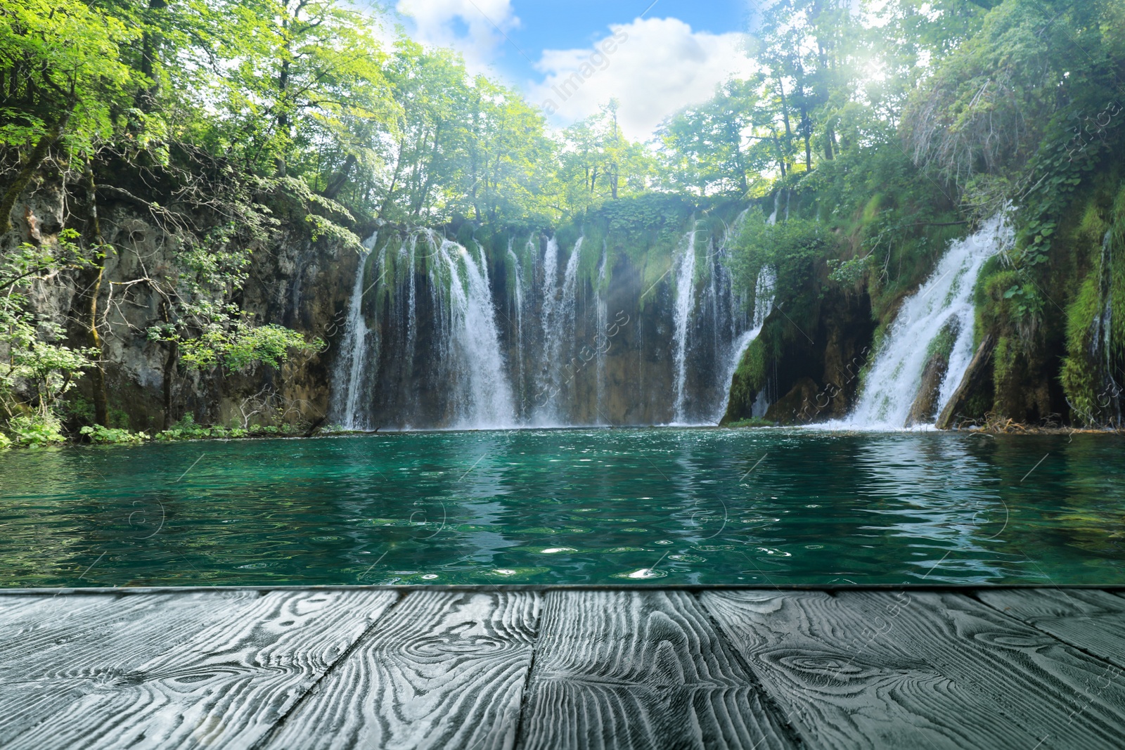 Image of Beautiful view of waterfall and wooden pier near lake on sunny day