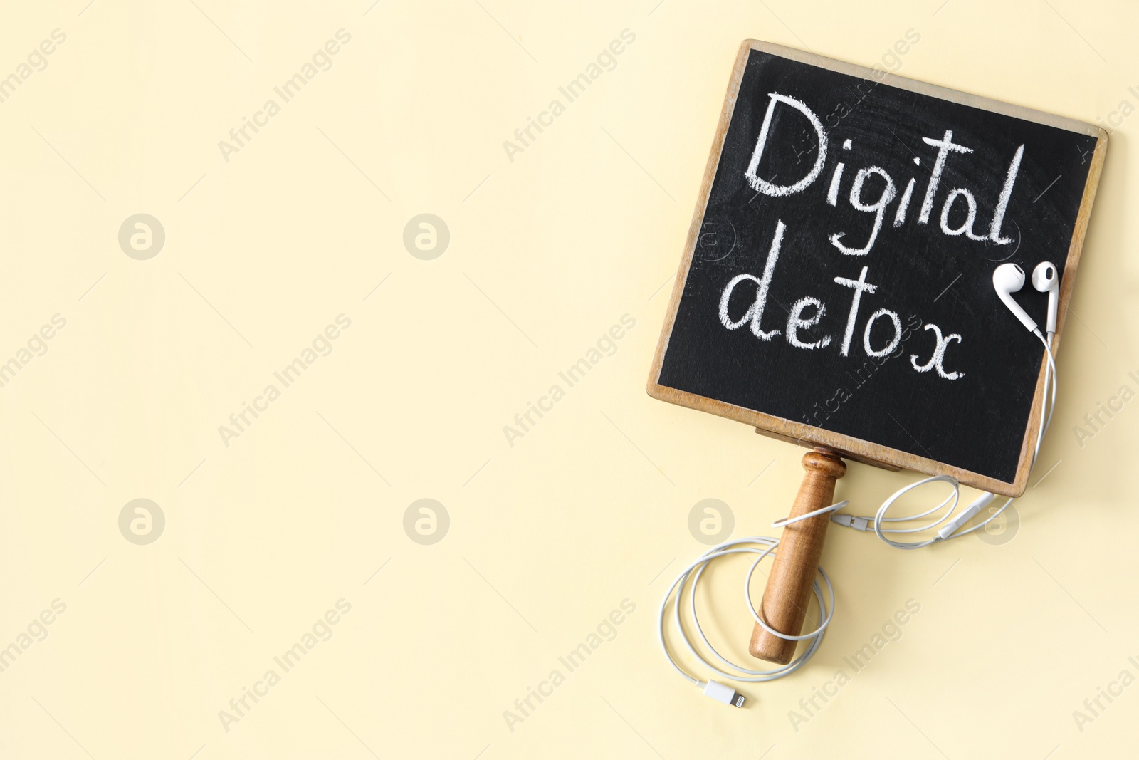 Photo of Blackboard plate with words DIGITAL DETOX and earphones on beige background, flat lay. Space for text