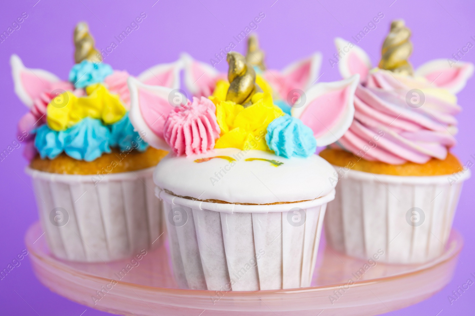 Photo of Plate with cute sweet unicorn cupcakes on violet background, closeup