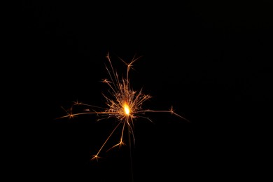 Photo of One burning sparkler stick on black background