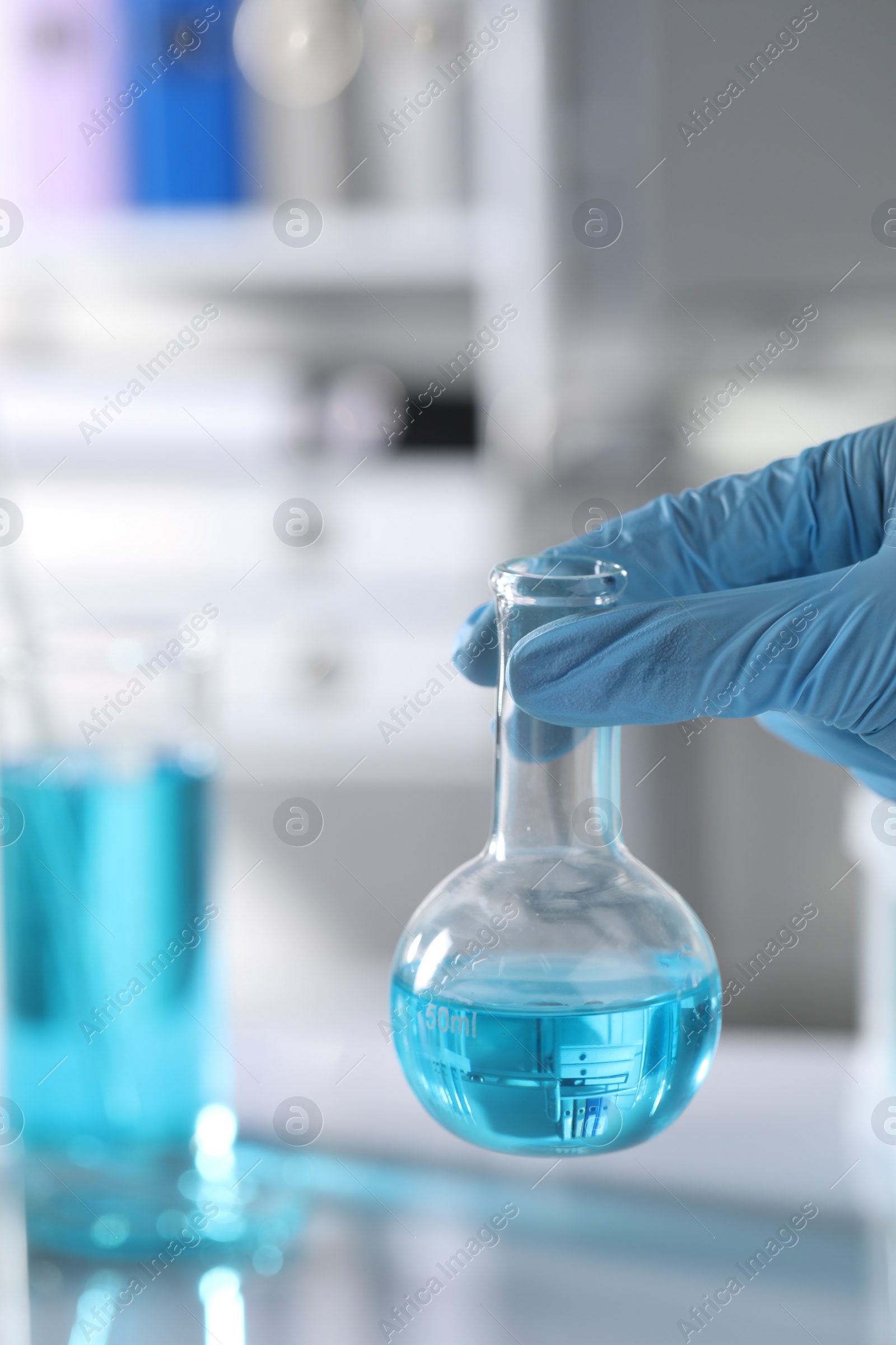 Photo of Scientist holding flask with light blue liquid in laboratory, closeup