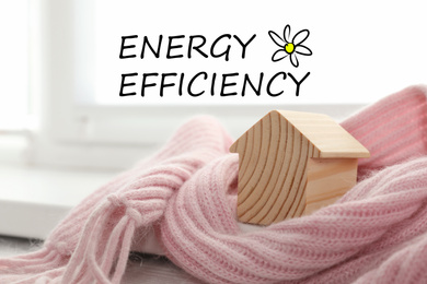 Image of Energy efficiency concept. Wooden house model wrapped in pink scarf on windowsill indoors