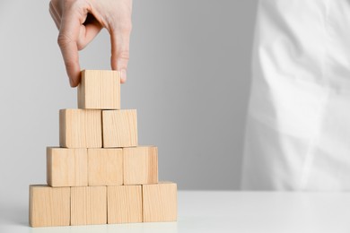 Photo of Woman building pyramid of blank wooden cubes on white table against light background, closeup. Space for text