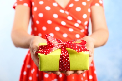 Woman holding beautifully wrapped gift box on color background