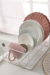 Drainer with different clean dishware and cup on light table indoors