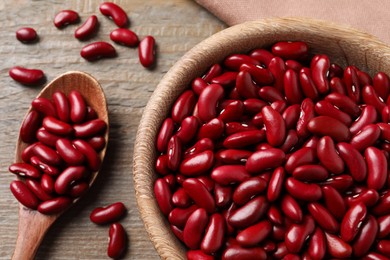 Photo of Raw red kidney beans with bowl and spoon on wooden table, flat lay