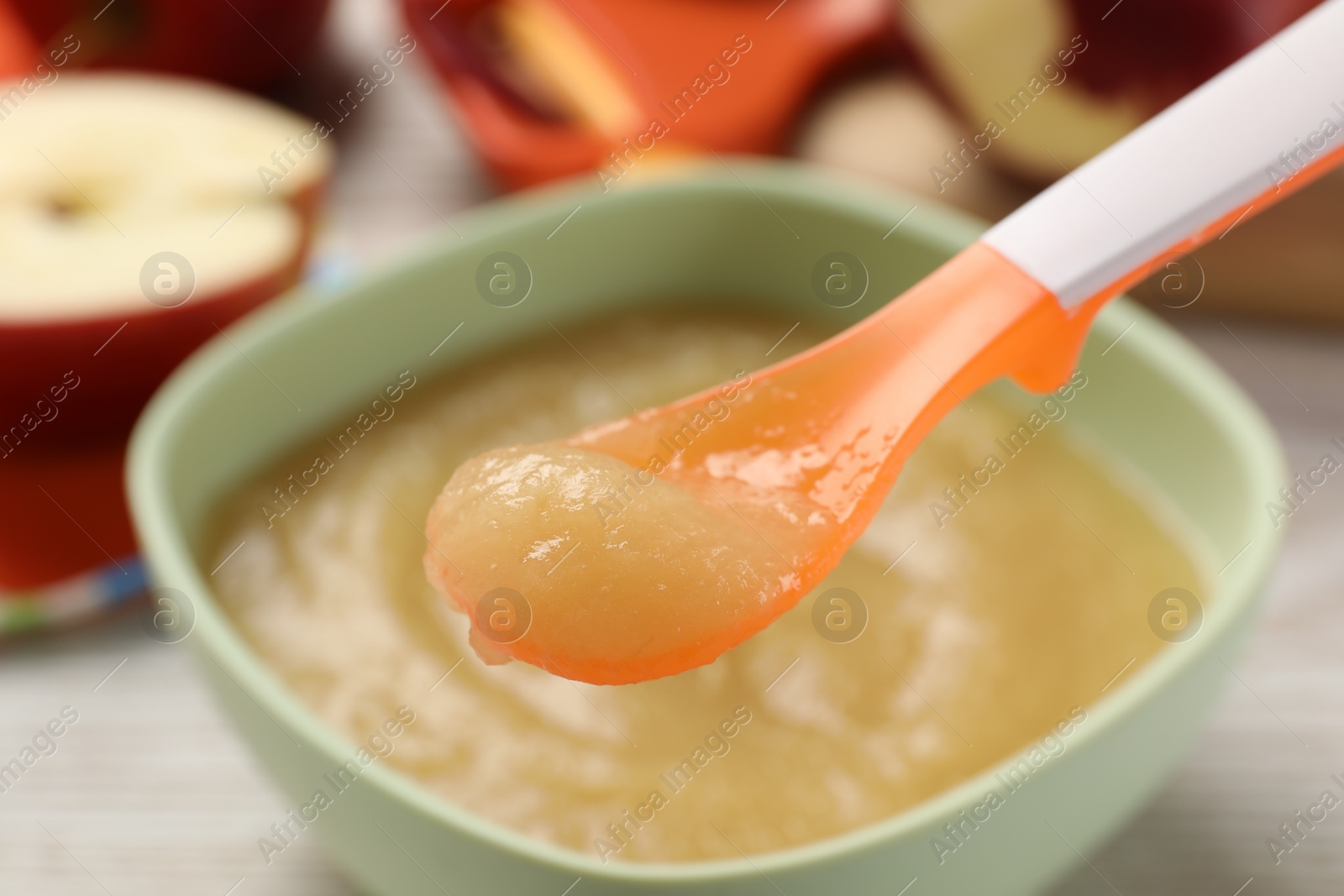 Photo of Healthy baby food. Spoon with delicious apple puree over bowl, closeup