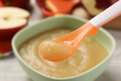 Healthy baby food. Spoon with delicious apple puree over bowl, closeup