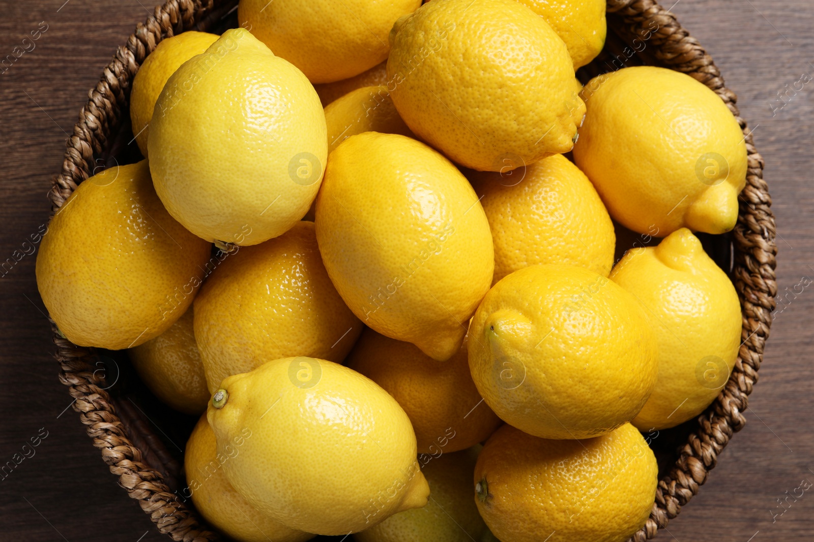 Photo of Fresh lemons in wicker basket on wooden table, top view