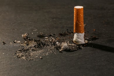 Burnt cigarette and ash on black table, closeup. No smoking concept