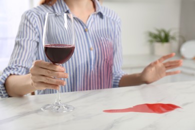 Woman with wine stain on her shirt at white marble table indoors, closeup