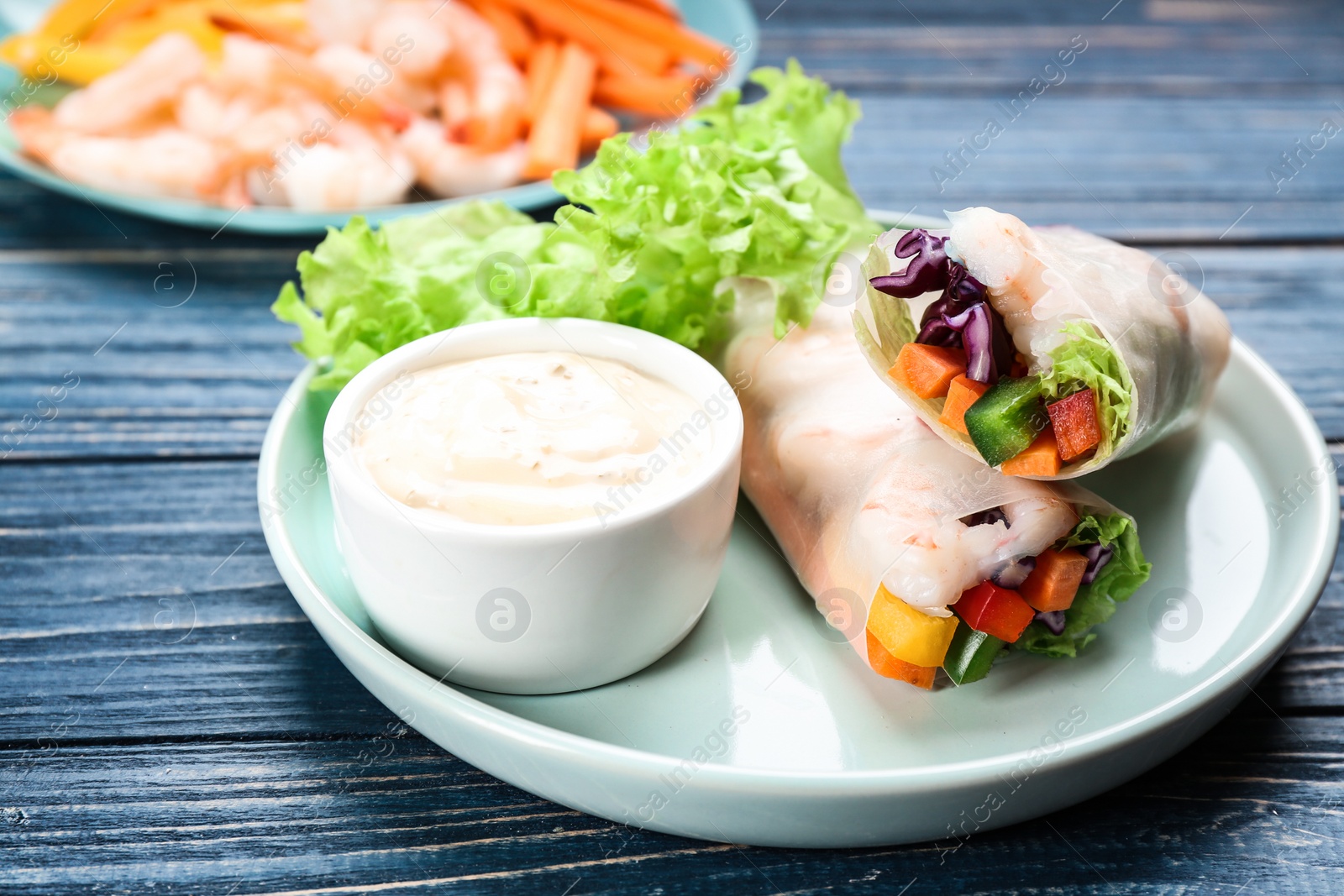 Photo of Delicious rolls wrapped in rice paper served on blue wooden table