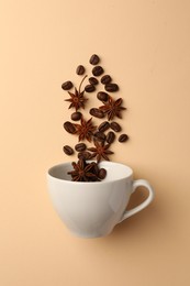Coffee beans and anise stars falling into cup on beige background, flat lay