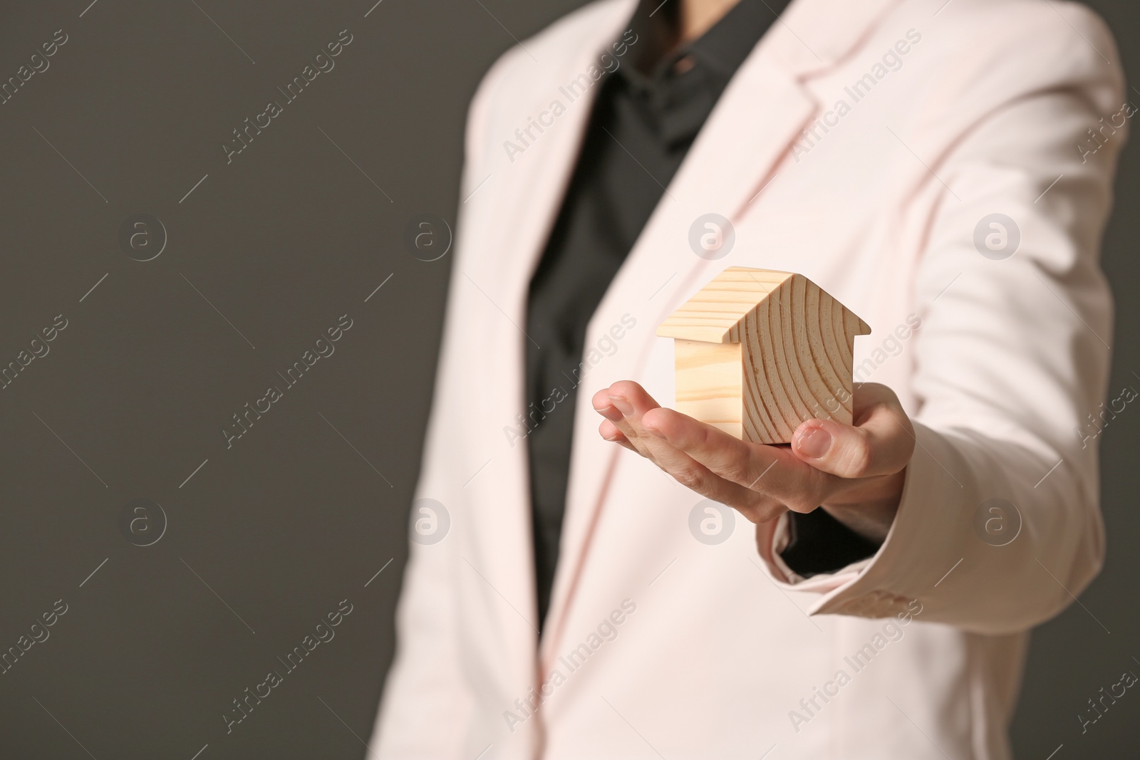 Photo of Female agent holding wooden house on dark background, closeup. Home insurance