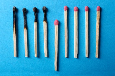 Photo of Burnt and whole matches on light blue background, flat lay. Stop destruction by breaking chain reaction concept