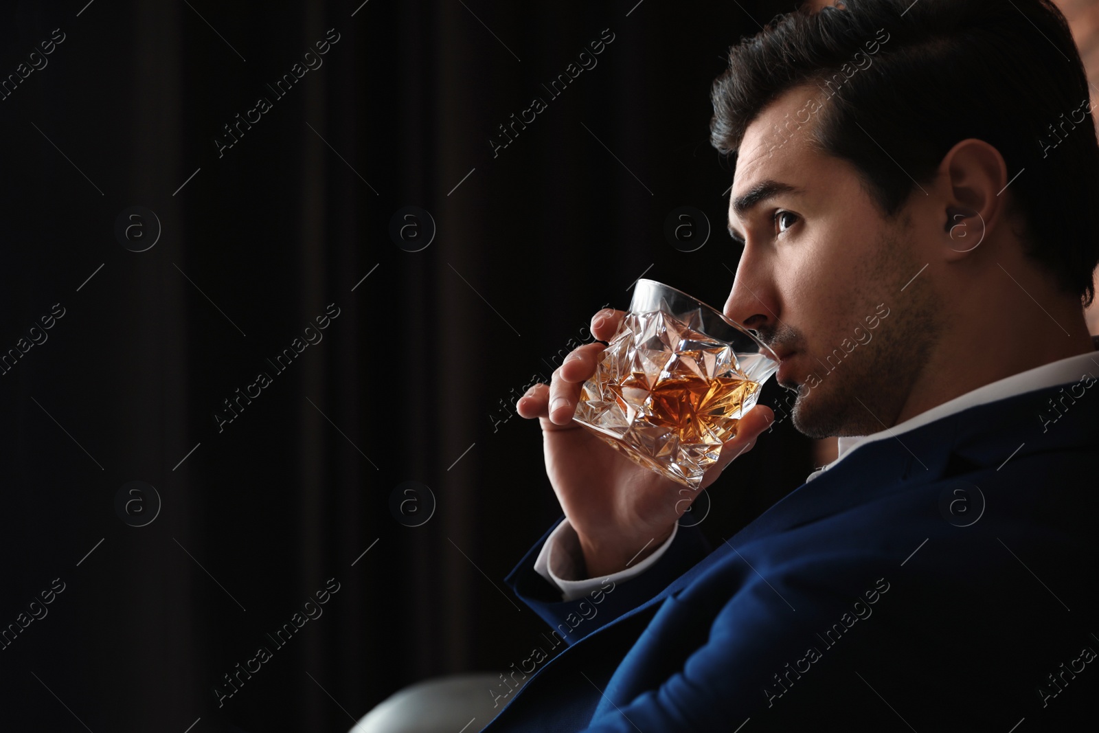 Photo of Young man with glass of whiskey indoors. Space for text