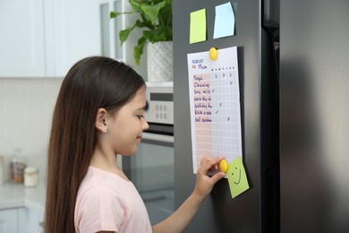 Little girl putting to do list on fridge in kitchen