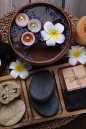 Different spa products, plumeria flowers and burning candles on wooden table, top view