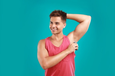 Young man applying deodorant to armpit on blue background