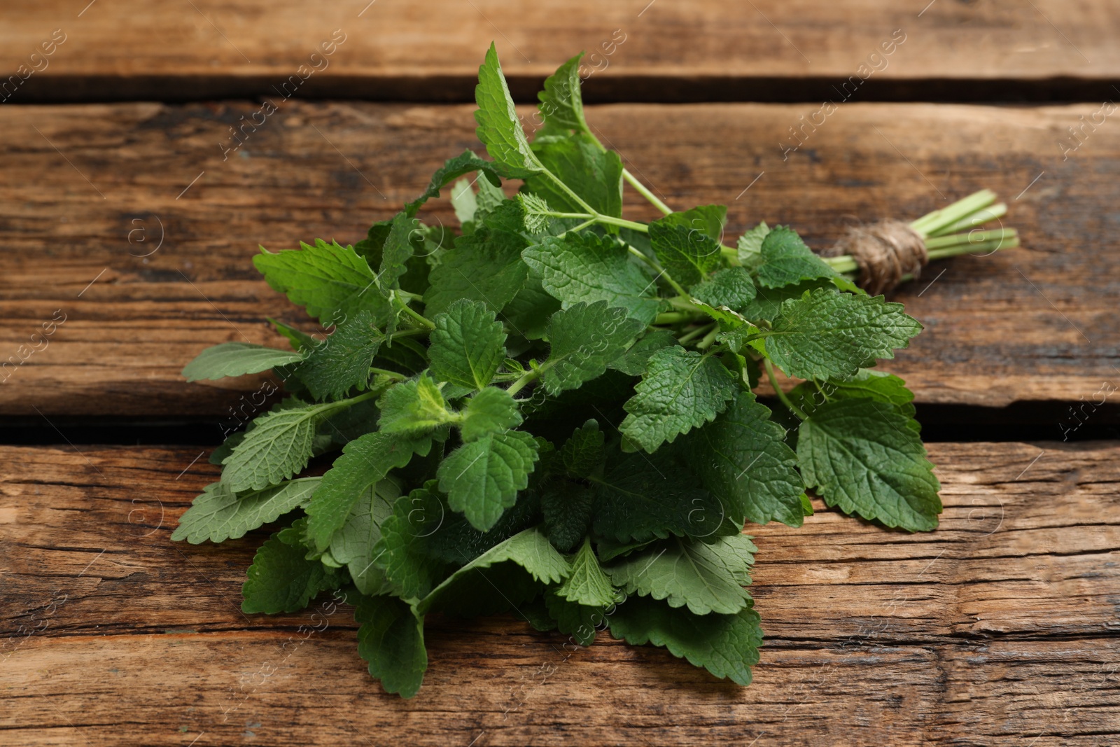 Photo of Bunch of fresh green lemon balm on wooden table, closeup