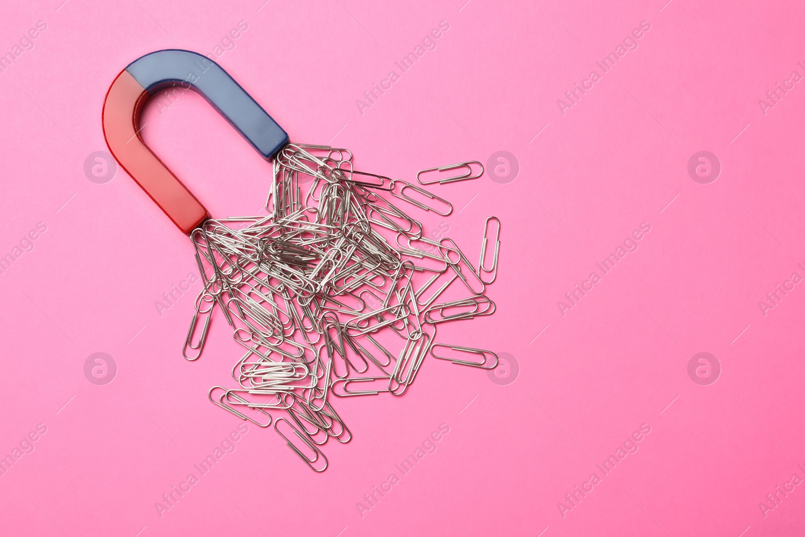 Photo of Magnet attracting paper clips on color background, top view with space for text