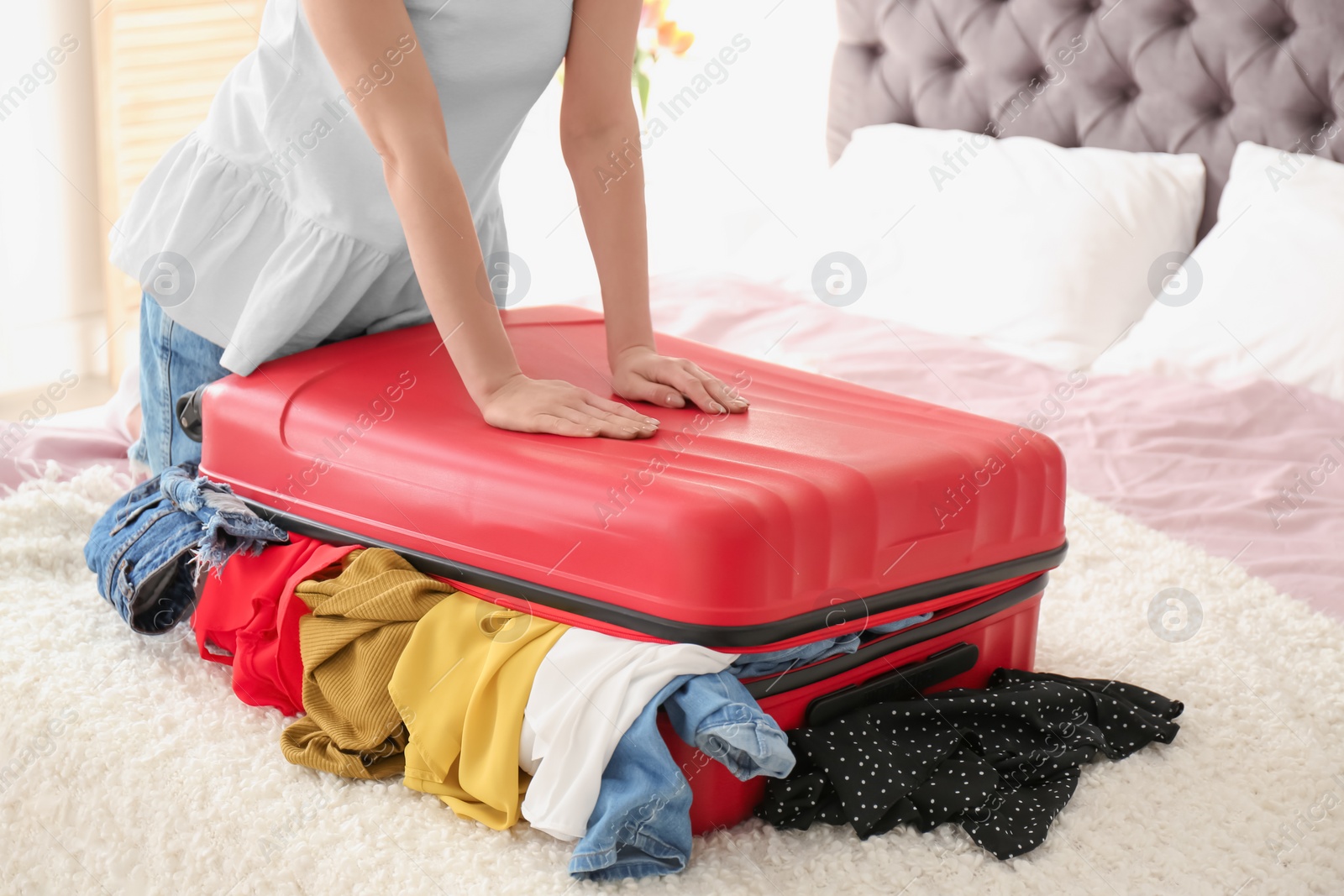 Photo of Young woman struggling to close suitcase on bed