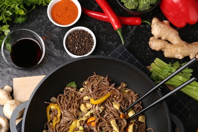 Photo of Stir-fry. Tasty noodles with meat and vegetables in wok served on dark textured table, flat lay