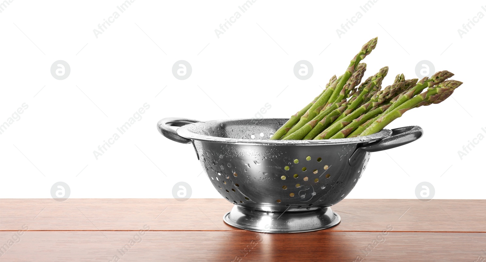 Photo of Metal colander with asparagus on wooden table against white background, space for text