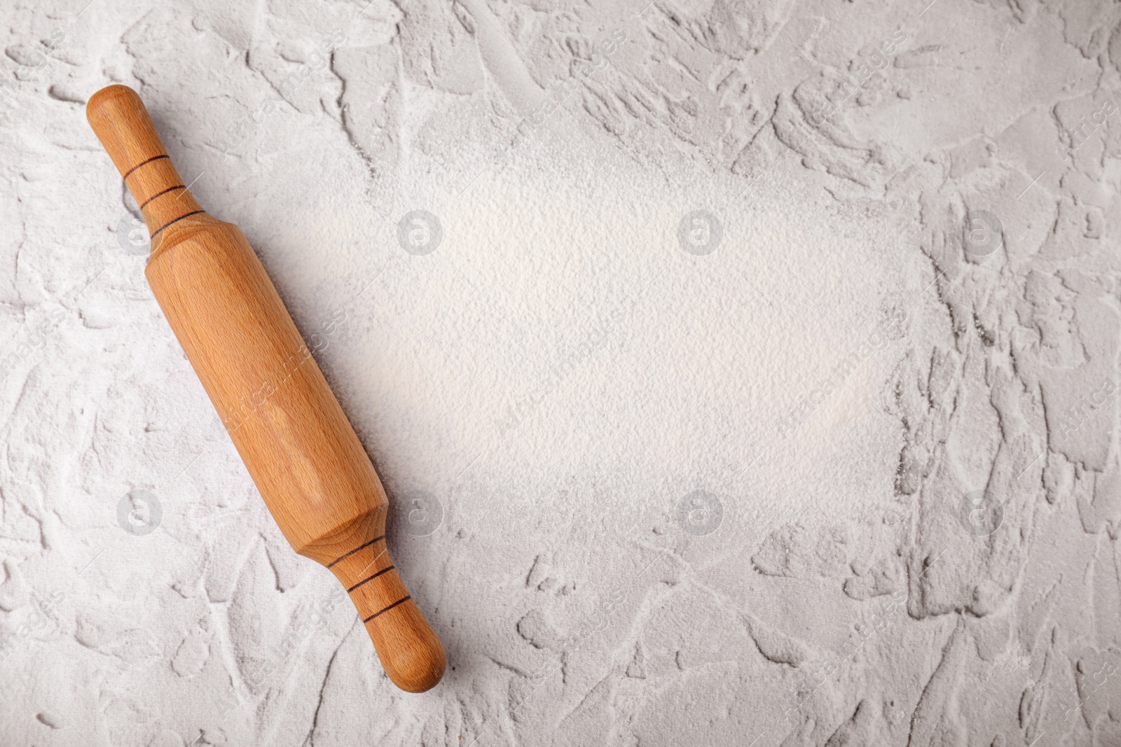 Photo of Flour and rolling pin on white textured table, top view