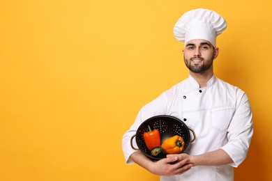 Professional chef holding colander with vegetables on yellow background. Space for text