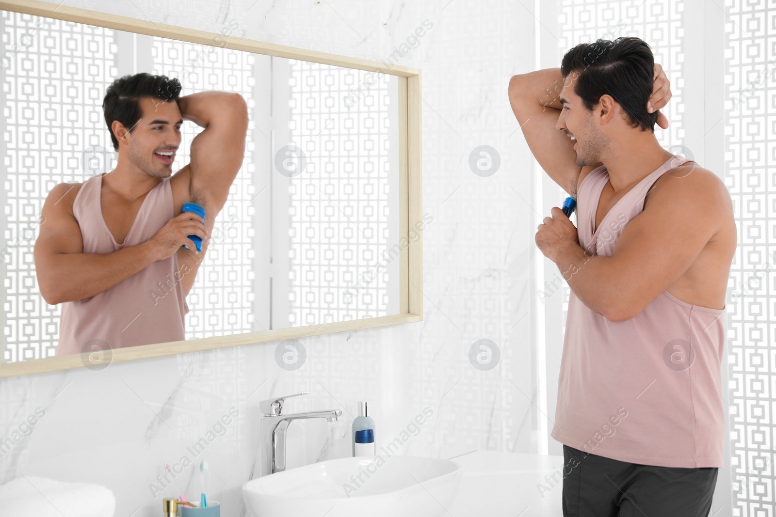 Photo of Handsome young man applying deodorant in bathroom