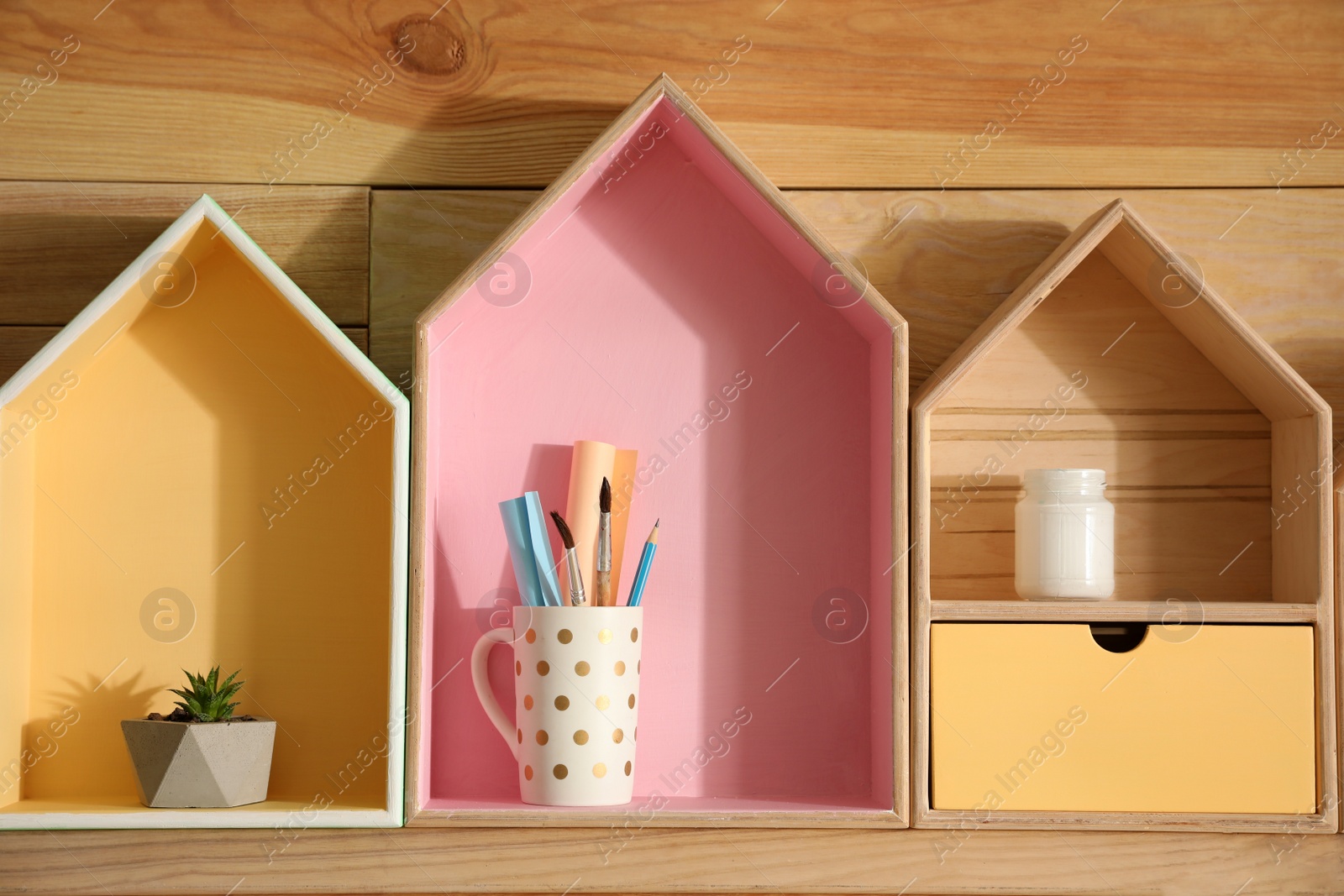 Photo of Painted house shaped shelves with different items on wooden wall. Interior elements