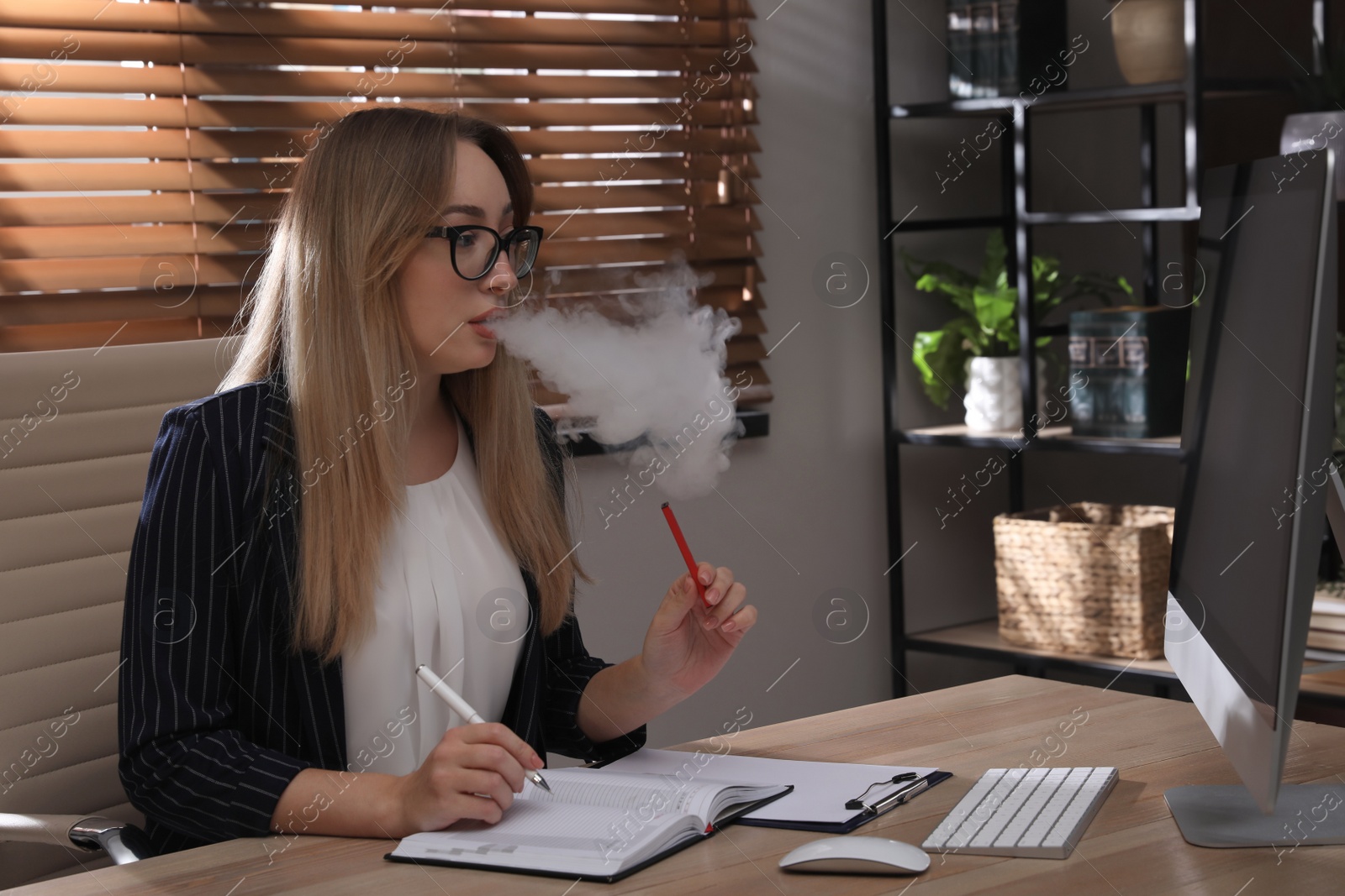 Photo of Beautiful young woman using disposable electronic cigarette at table in office