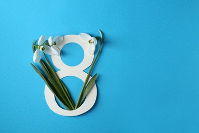 Photo of Beautiful snowdrops and paper number 8 on light blue background, flat lay. Space for text