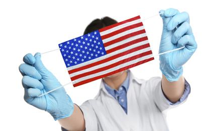 Doctor holding medical mask with USA flag pattern on white background. Dangerous virus