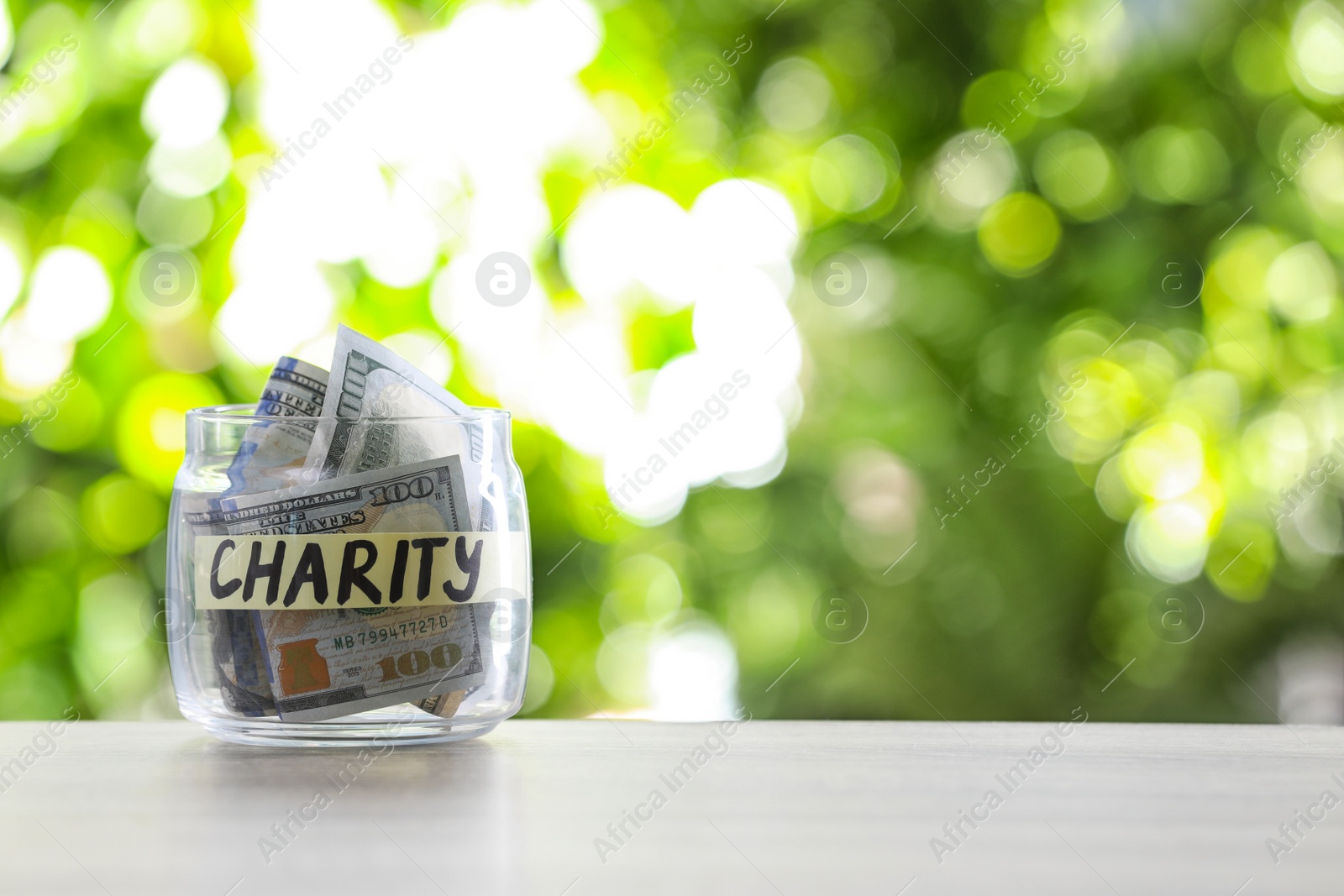 Photo of Glass jar with money and label CHARITY on table against blurred background. Space for text