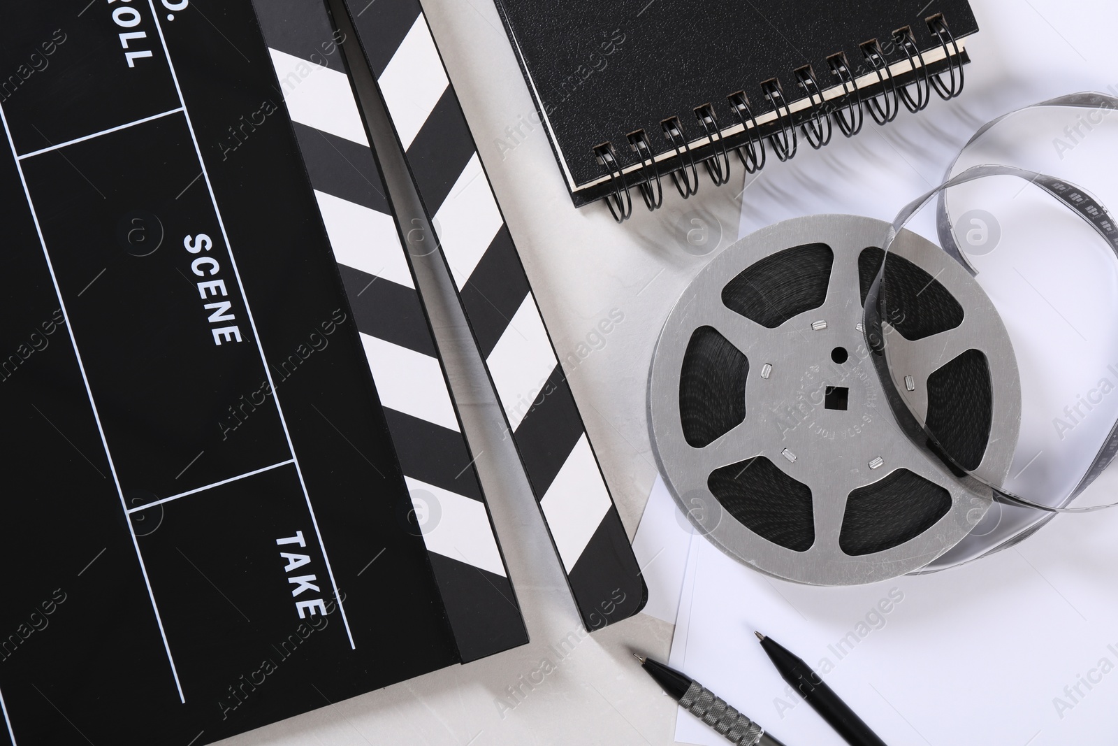 Photo of Movie clapper, film reel, notebook and pens on light table, flat lay