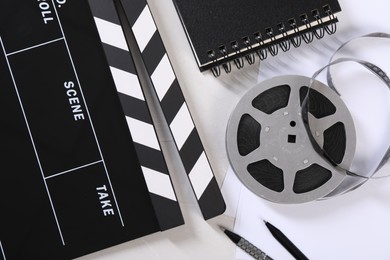 Movie clapper, film reel, notebook and pens on light table, flat lay