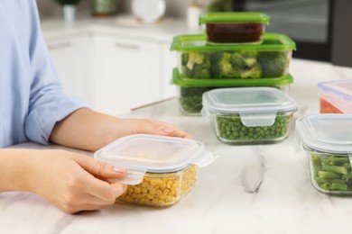 Photo of Woman sealing container with corn at white marble table in kitchen, closeup. Food storage